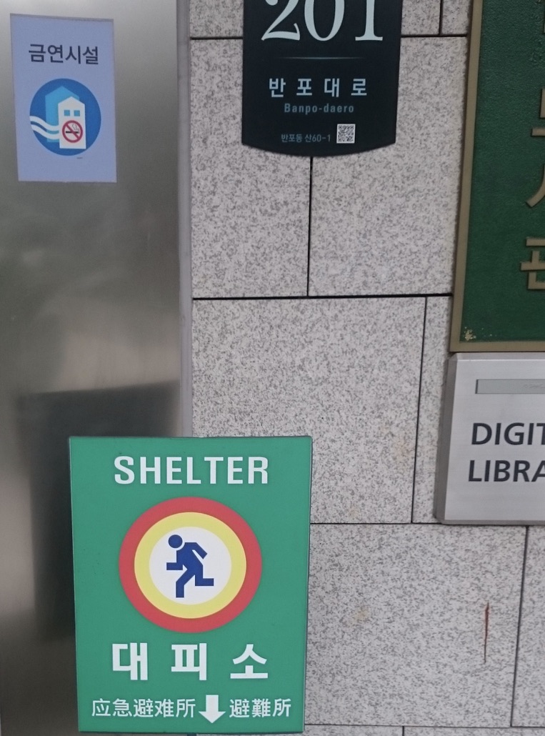 人が走る絵を黄色と赤で丸しているピクトグラム。朝鮮語、英語、漢語、日本語で表示。